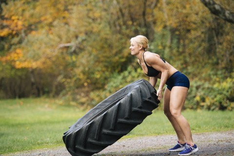Caucasian woman lifting heavy tire in park
