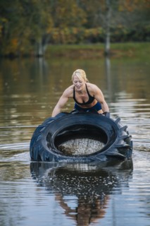 Caucasian woman lifting heavy tire in lake
