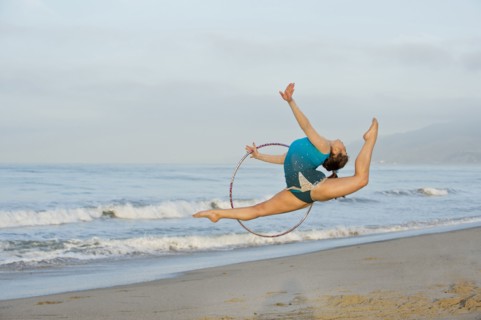 Caucasian gymnast jumping with hoop on beach