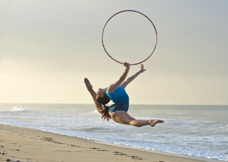 Caucasian gymnast jumping with hoop on beach
