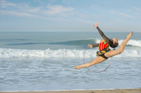 Caucasian gymnast jumping with hoop on beach
