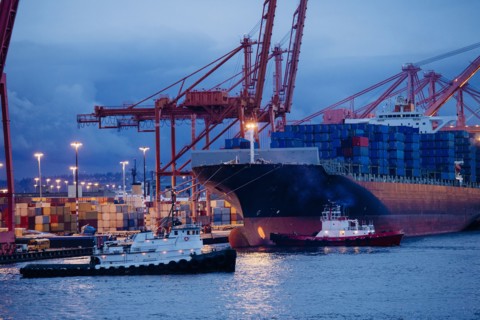 Cargo containers on freighter at shipping port near tugboats