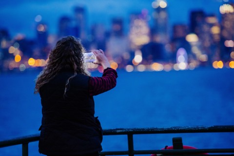Caucasian woman on boat photographing urban waterfront with cell phone