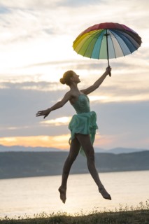 Caucasian ballerina jumping with multicolor umbrella on beach