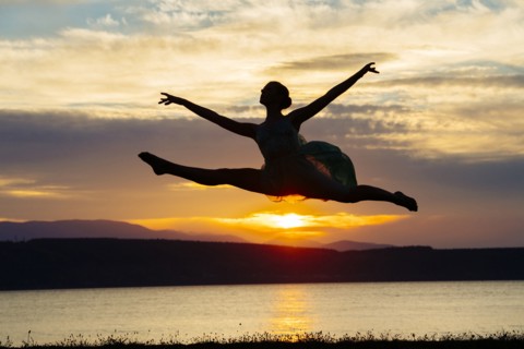 Caucasian ballerina jumping on beach at sunset