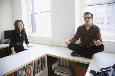Hispanic businessman meditating next to coworker