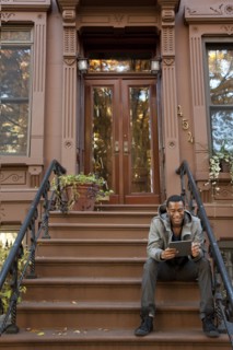 Black man sitting on front stoop using digital tablet