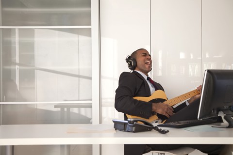 Black businessman playing guitar at desk