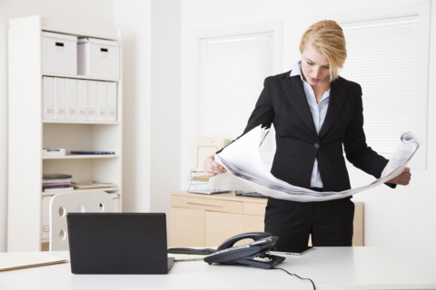 Caucasian businesswoman reading blueprints in office