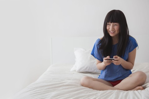 Chinese woman using cell phone on bed