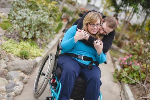 Man hugging paraplegic girlfriend in garden