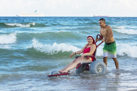 Man pushing paraplegic girlfriend in wheelchair on beach