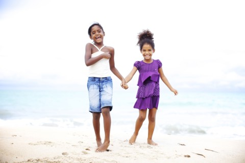 Mixed race sisters holding hands on beach