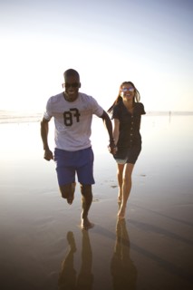 Happy couple holding hands and running on beach