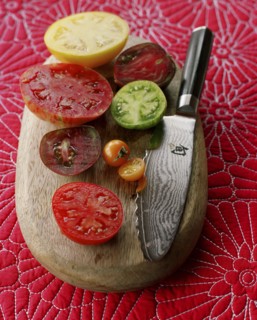 Various juicy sliced tomatoes on cutting board with knife