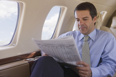 Hispanic businessman reading newspaper on airplane