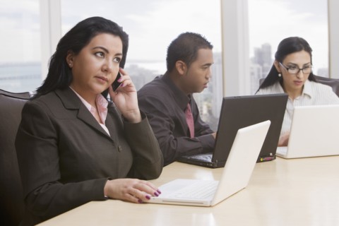 Business people in meeting using cell phone and laptops