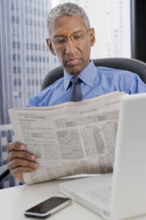 Mixed race businessman reading newspaper at desk