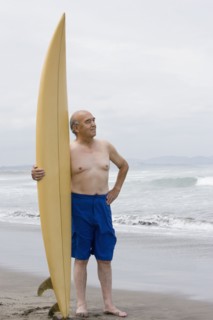 Senior Hispanic man holding surfboard on beach