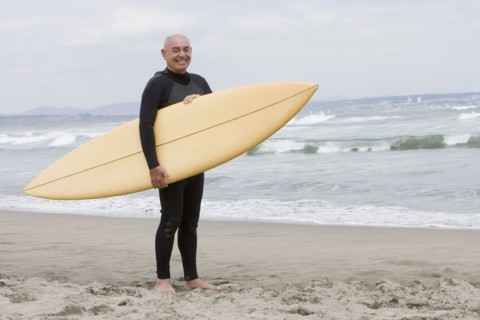 Senior Hispanic man holding surfboard on beach