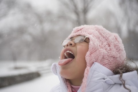 Hispanic girl catching snowflakes on tongue