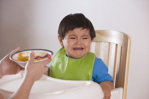 Hispanic mother trying to feed crying baby boy