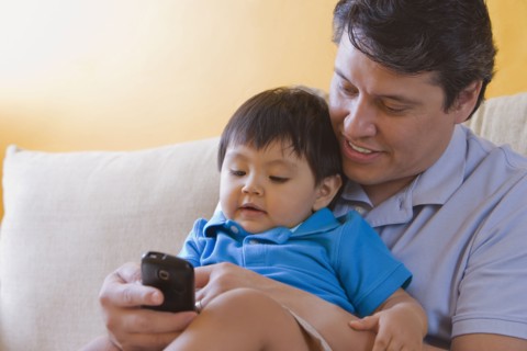 Hispanic father showing cell phone to his son