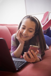 Hispanic girl using laptop and cell phone on sofa