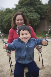 Hispanic mother pushing son on swings
