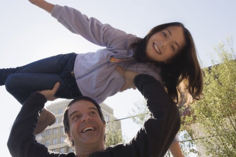 Hispanic man lifting daughter over his head