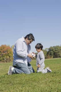 Hispanic father and son playing soccer outdoors