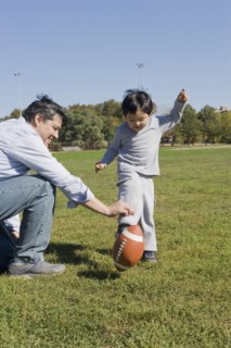 Hispanic father and son playing football outdoors