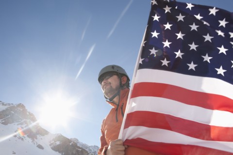 Hispanic hiker planting American flag on snowy mountain