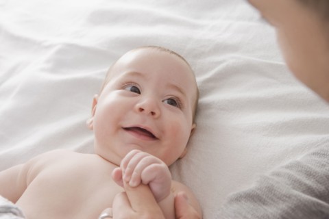 Father admiring Hispanic baby boy on bed