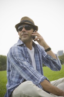 Hispanic man talking on cell phone in grass at park