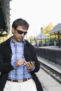 Hispanic man text messaging on train station platform
