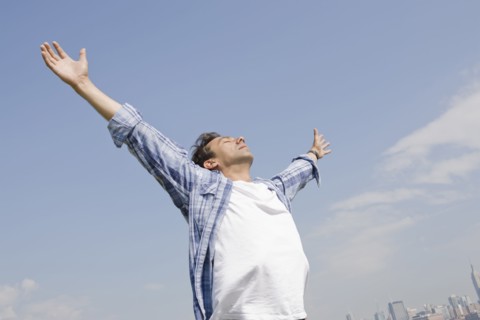 Hispanic man standing with arms outstretched against blue sky