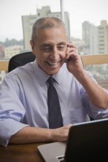 Hispanic businessman using cell phone and laptop in office