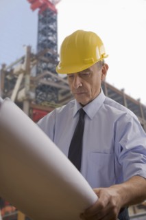Hispanic architect reviewing blueprints at construction site