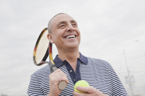 Hispanic senior man carrying tennis racket and ball