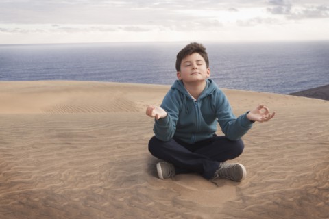 Hispanic boy meditating on sand dune over ocean