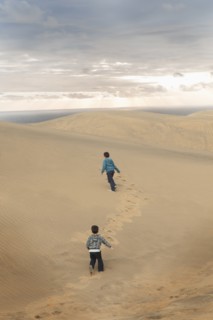 Hispanic brothers running on sand dunes