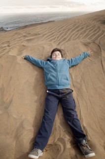 Hispanic boy laying on sand dune at beach