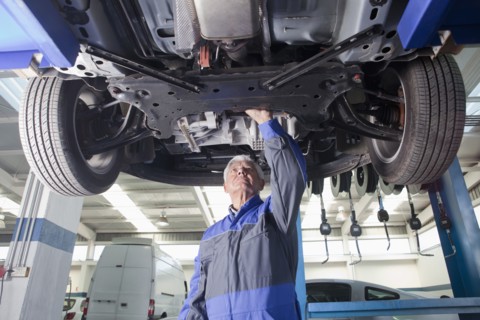 Older Hispanic mechanic repairing car in garage