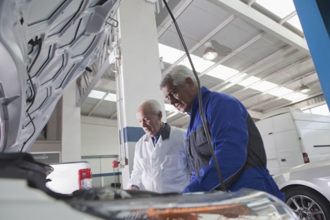 Older Hispanic mechanics repairing car in garage