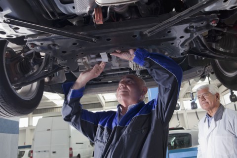 Older Hispanic mechanic repairing car in garage