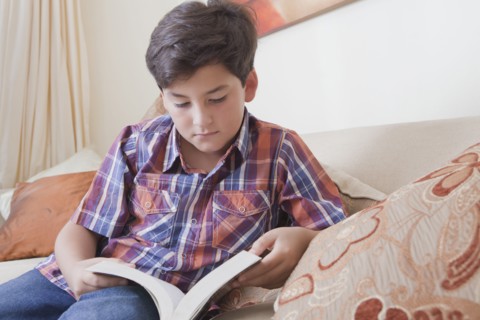 Hispanic boy reading book on sofa