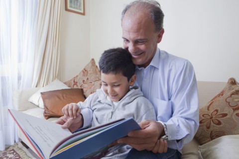 Hispanic father and son reading book on sofa