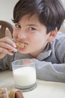Hispanic boy eating cookie with milk at table