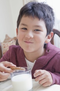 Hispanic boy eating cookie with milk at table